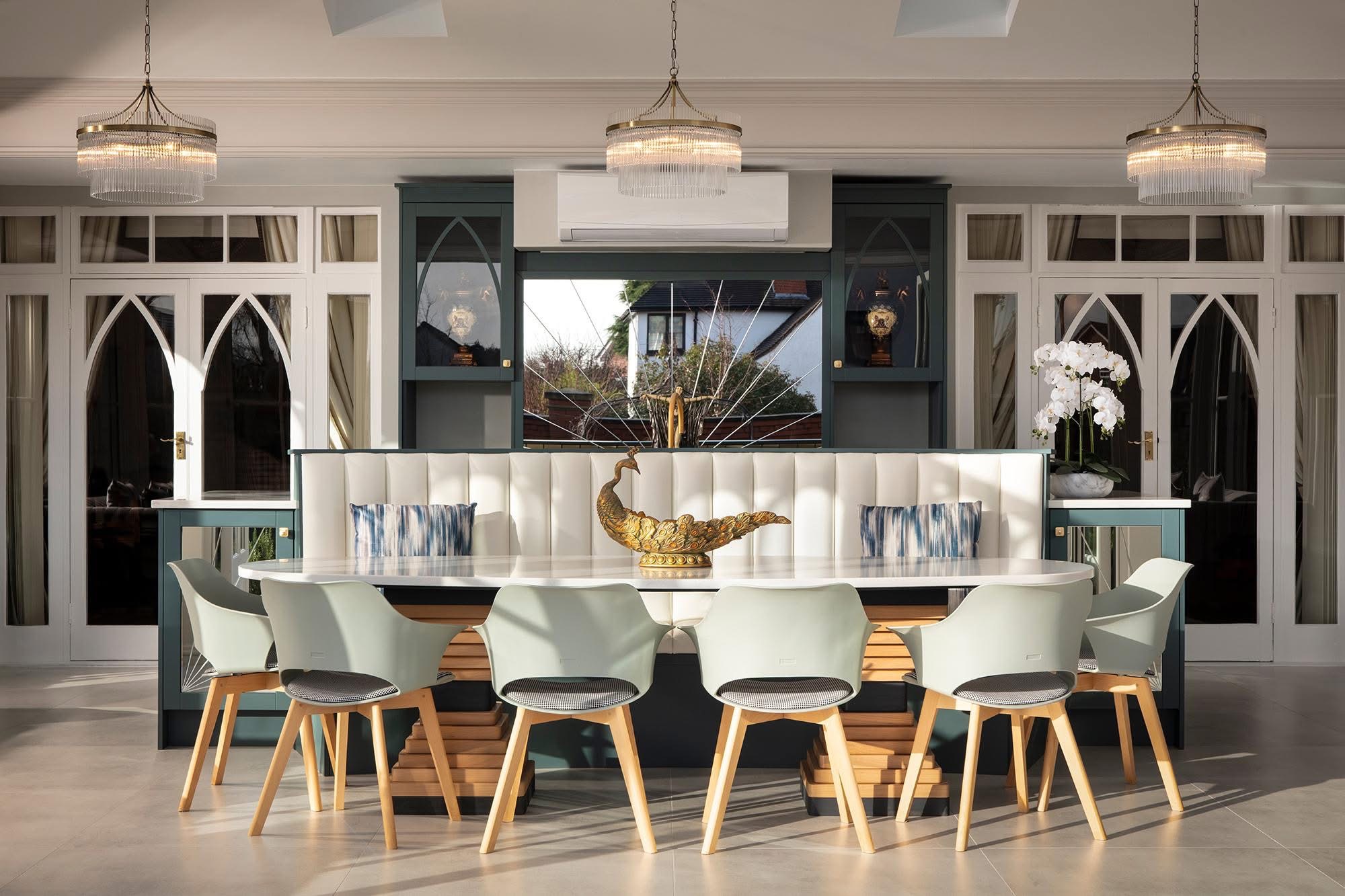 Deep teal painted kitchen with an oval dining table, cream fluted banquette and arch-glazed display cabinets