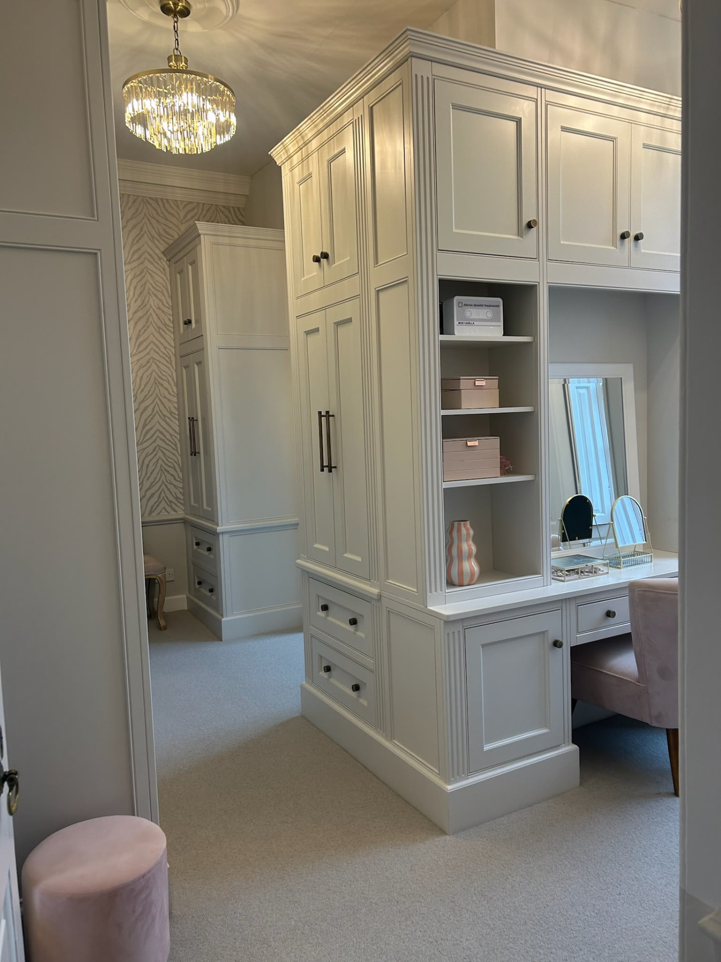 Cream fitted dressing room with floor-to-ceiling wardrobe towers, a built-in vanity and a blush velvet chair