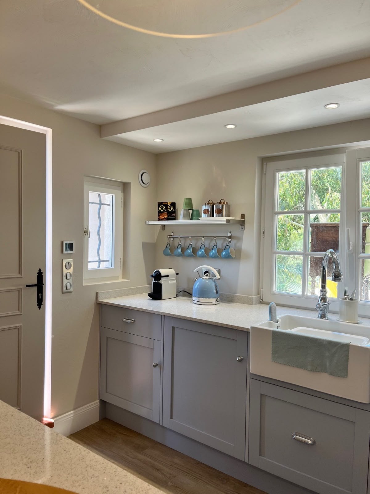 Painted shaker cabinets and an apron sink beside a garden door in a light-filled kitchen