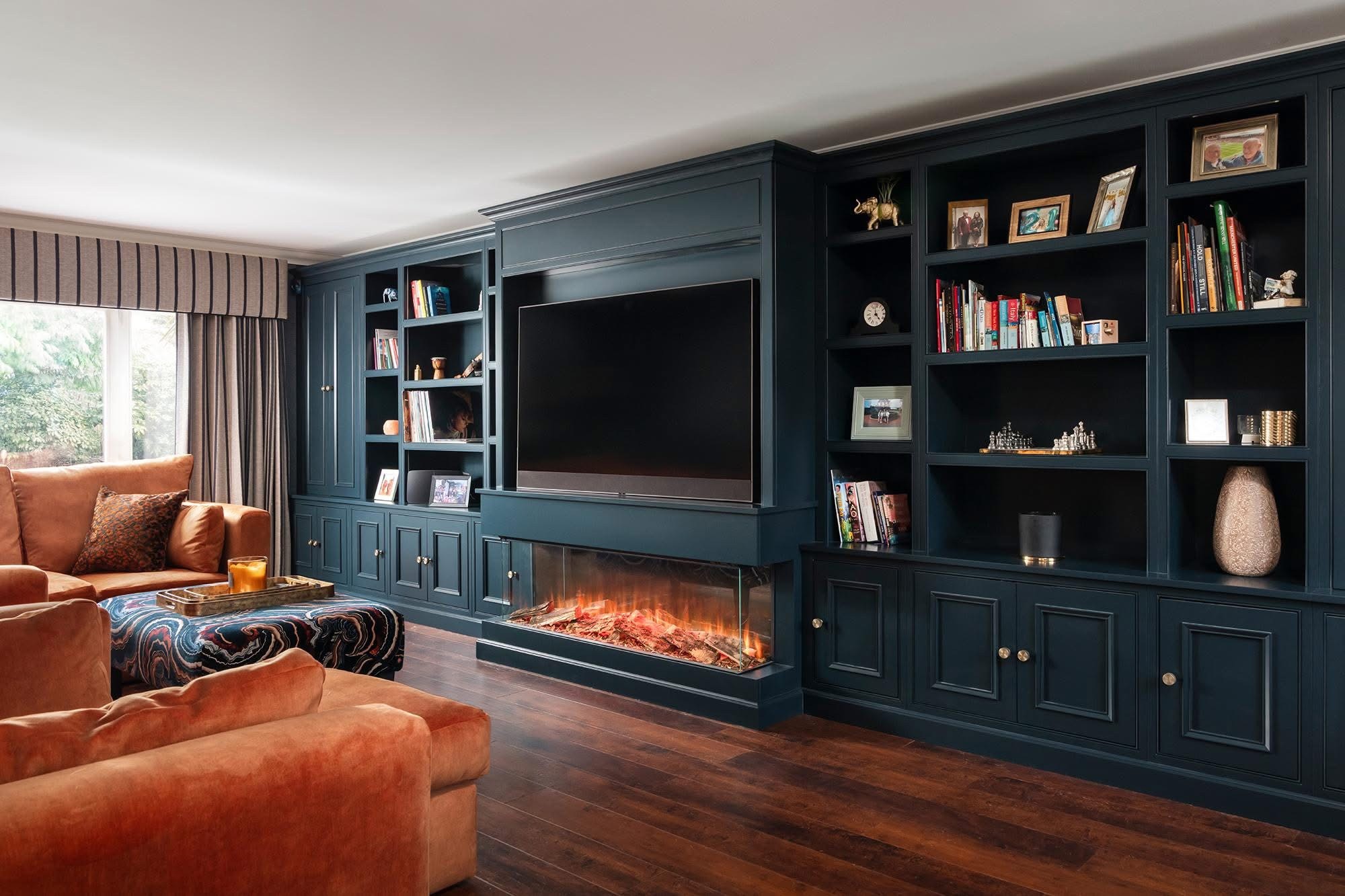Deep blue fitted media wall with television, open shelving and a long inset fireplace