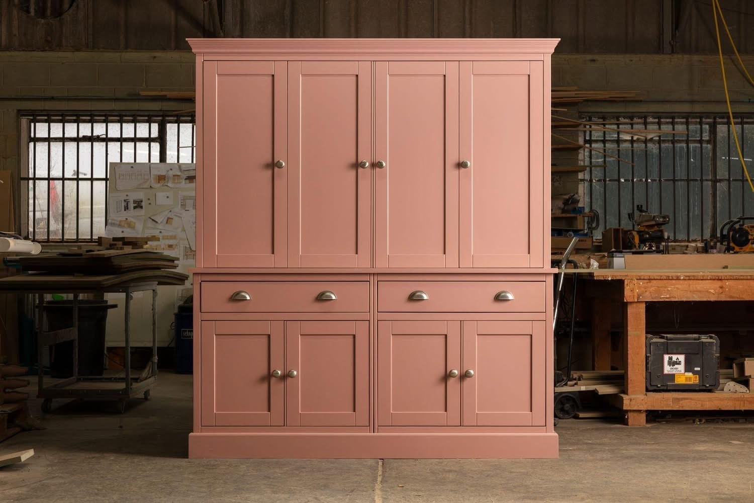 Freestanding pink painted cabinet with brass handles and drawers in the Elms Farm workshop